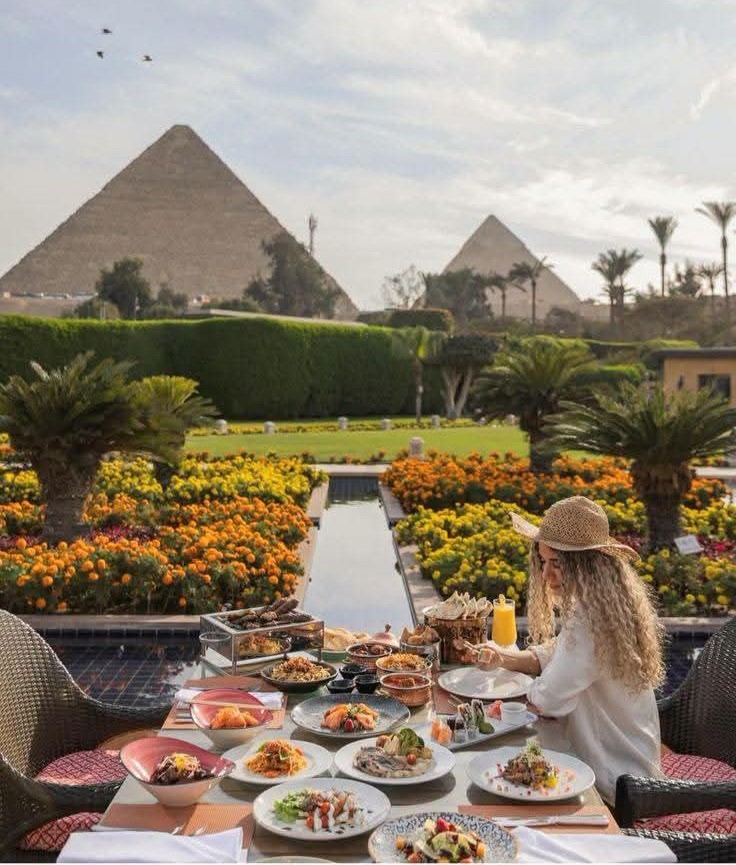 Breakfast laid out beside a pool with the pyramids rising behind