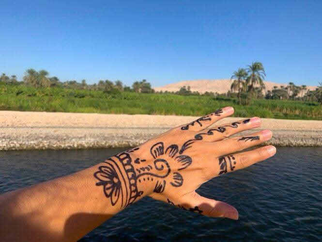 A henna-decorated hand raised against the Nile and palm groves